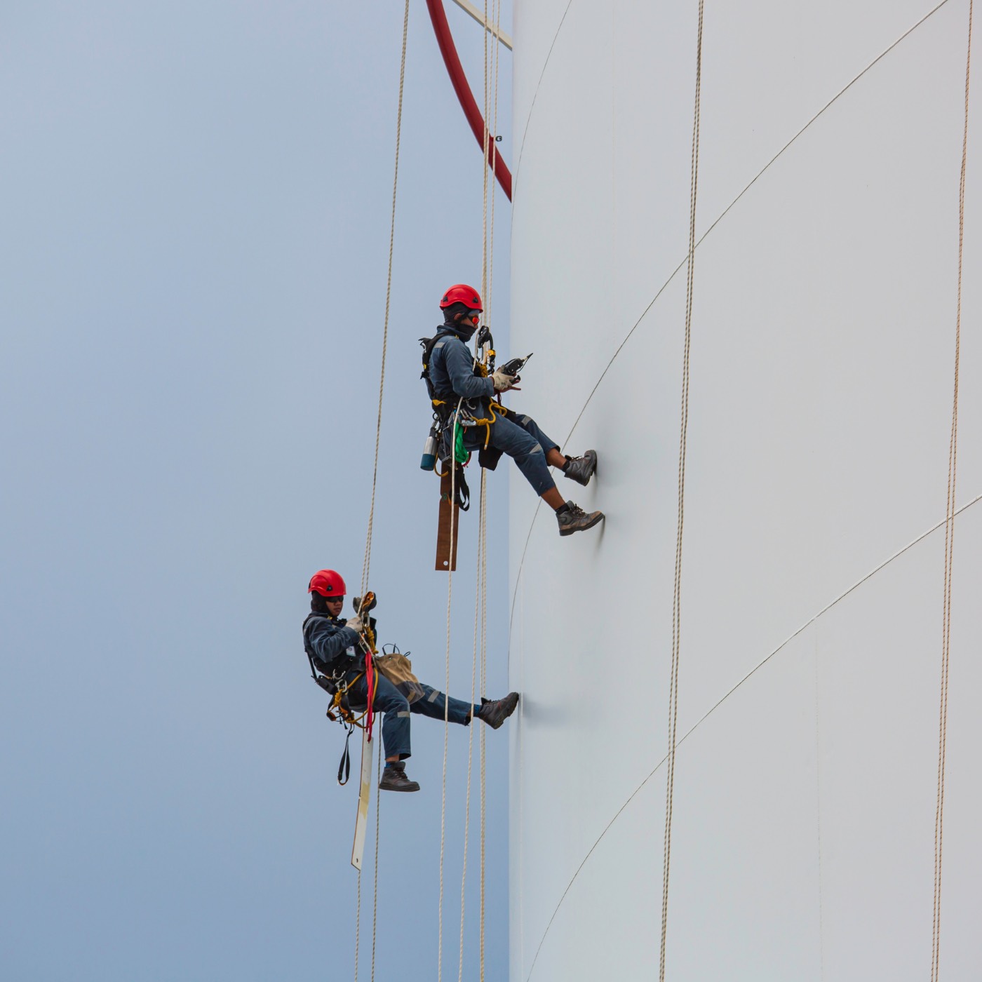 Two rope access technicians working on the side of a large white tank